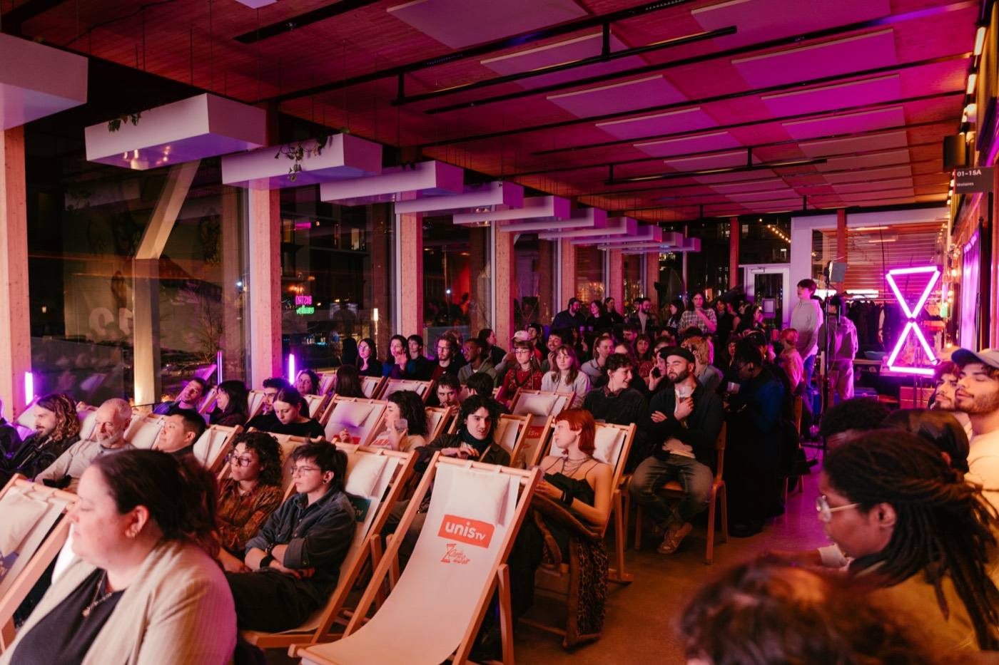Le public du festival Courts d’un Soir installé dans des chaises longues devant un écran, sous les néons roses.